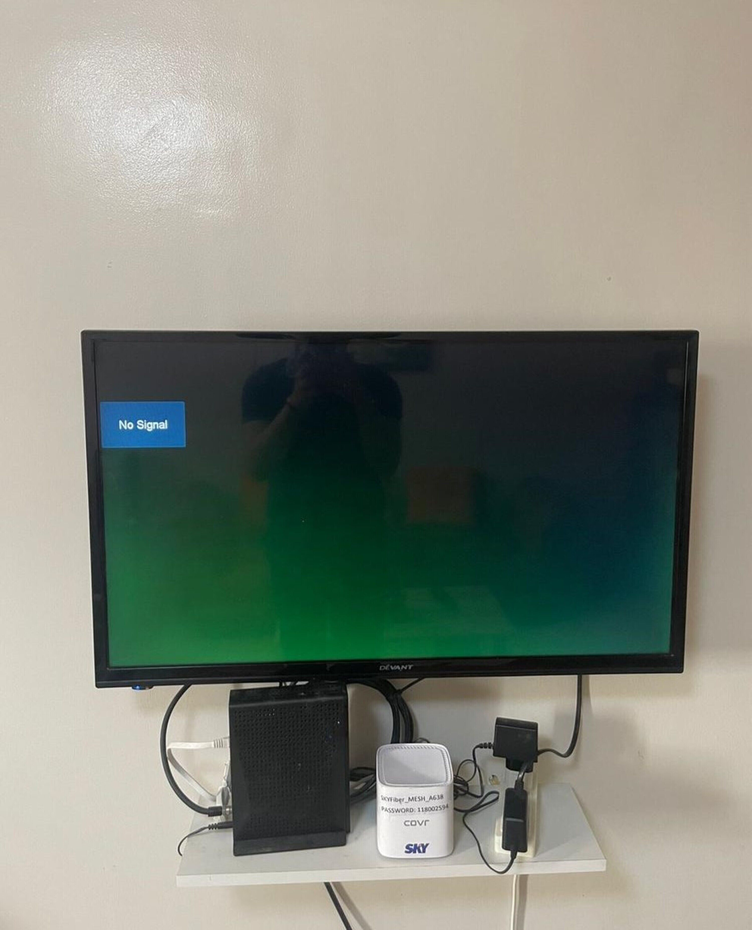 A flat-screen TV mounted on a white stand with a "No Signal" message, a black speaker, and a white device with cables.