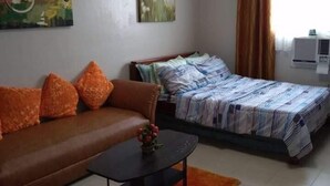 Una habitación con un sofá marrón, una cama con edredón a rayas, una mesita con un florero y un cuadro en la pared.
