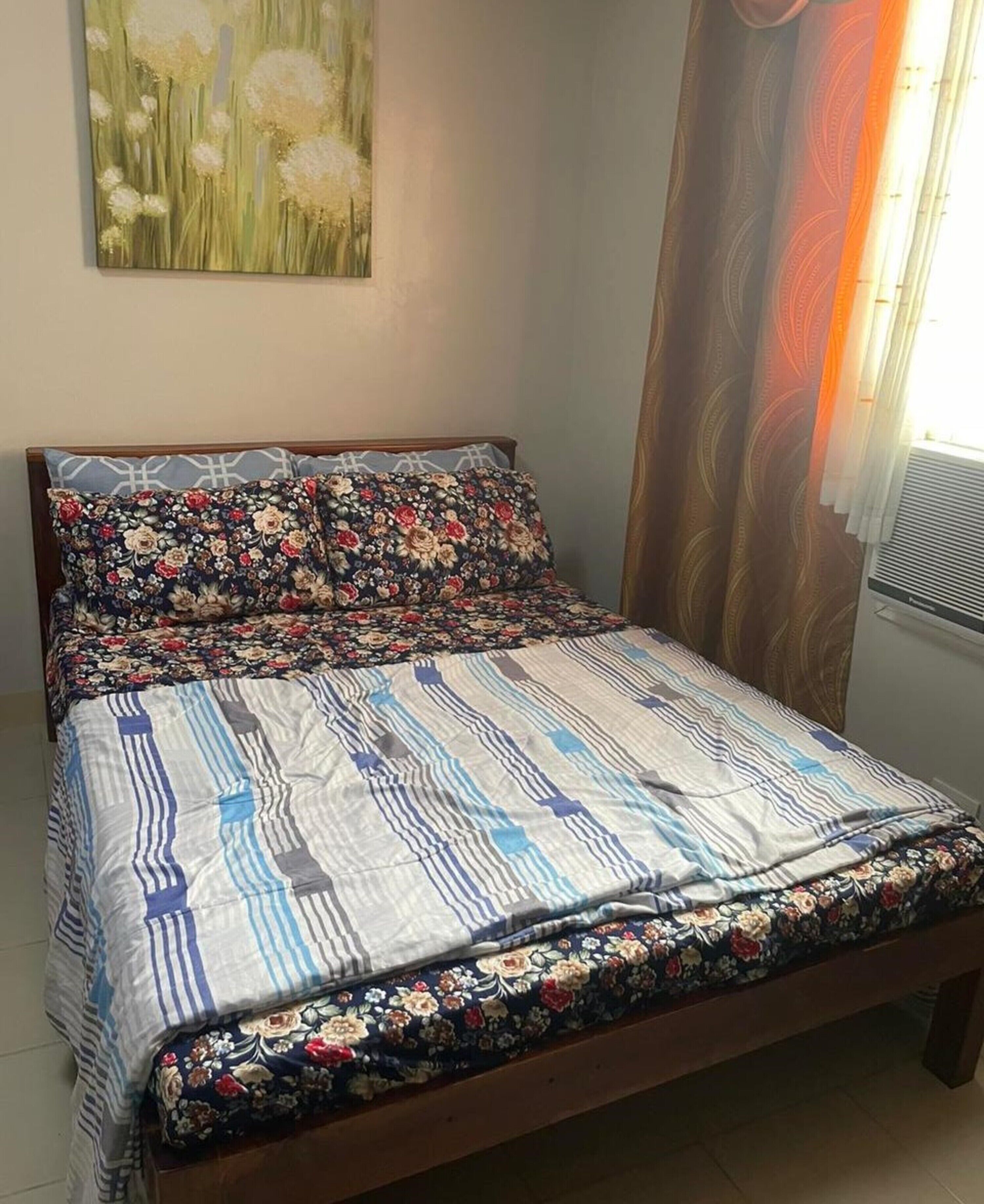 Una cama con ropa de cama floral y a rayas, un cabecero de madera y una obra de arte colgada en la pared.