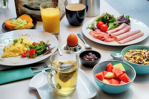 Una mesa de desayuno con platos de comida, un vaso de jugo, una taza y tazones de fruta y cereal.