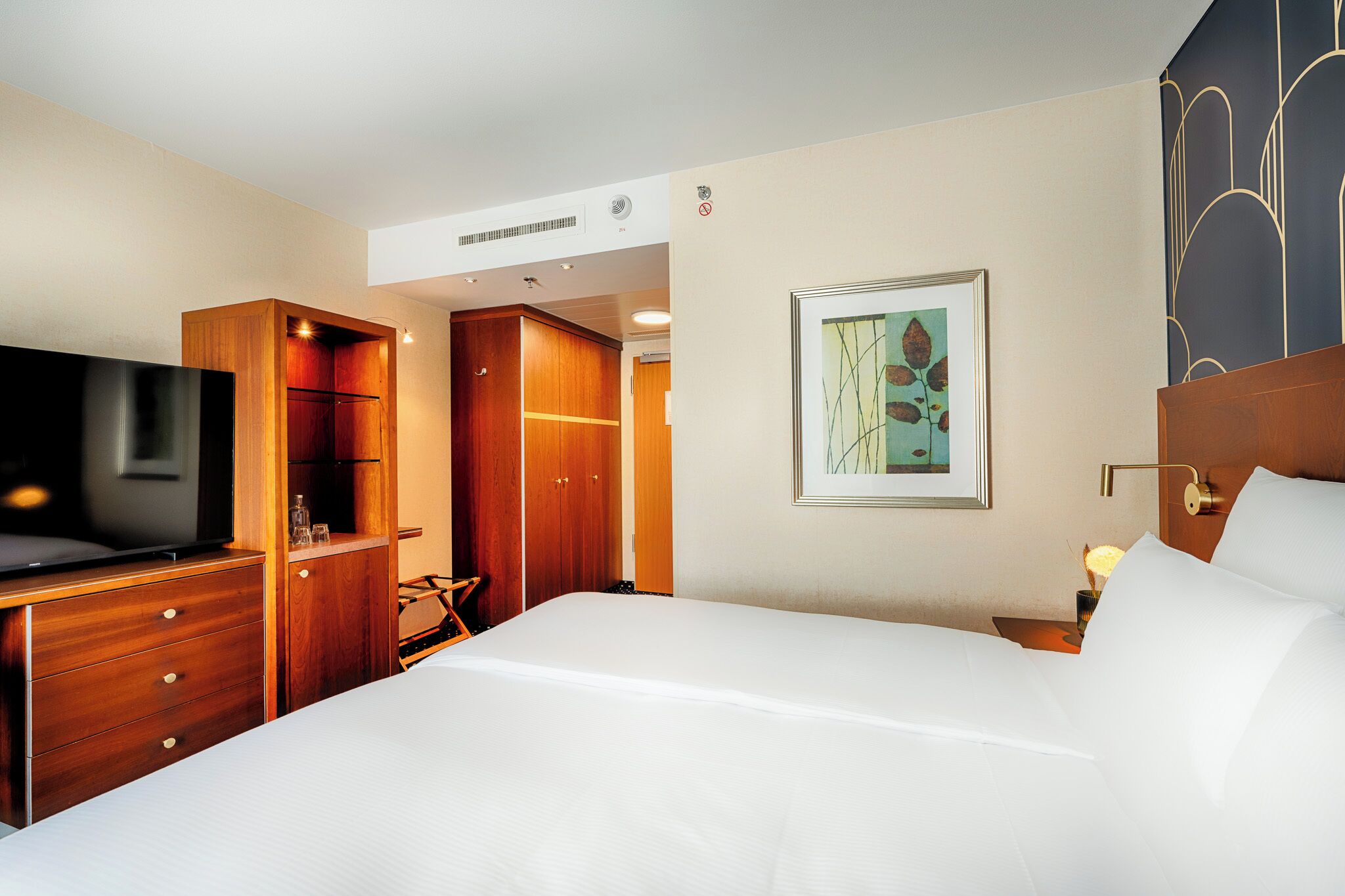 A hotel room with a bed, a TV, a wardrobe, and a framed picture on the wall.