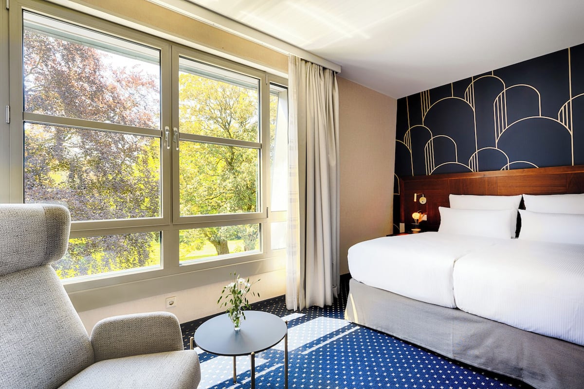 Een hotelkamer met een bed, een stoel, een klein tafeltje en een raam met gordijnen.