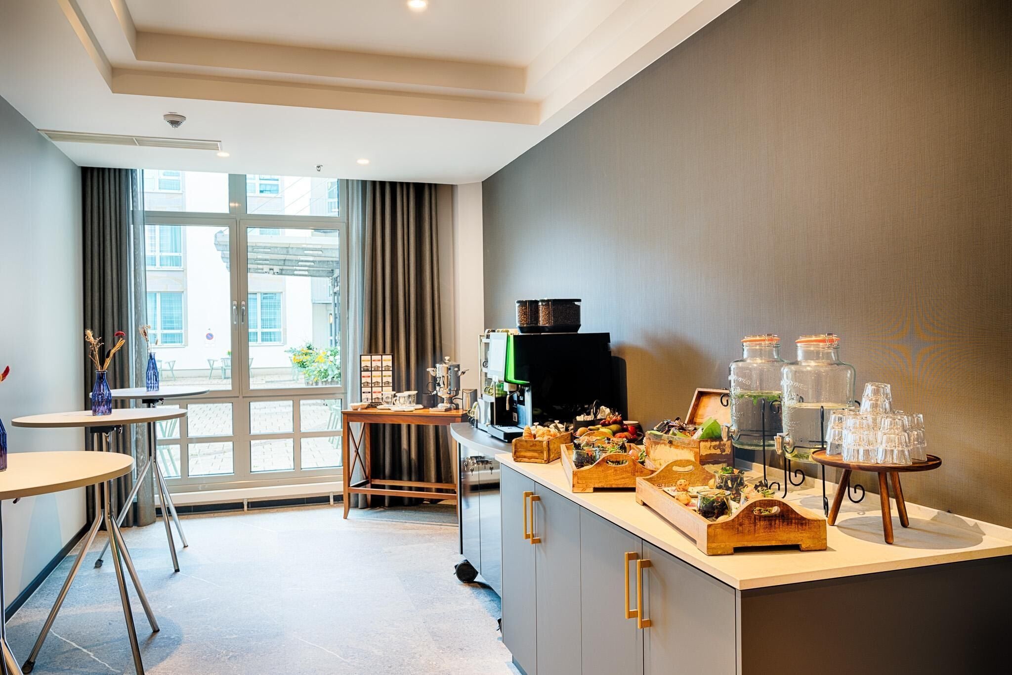 A modern kitchen with a large window, a coffee station, and a buffet area with various food items.