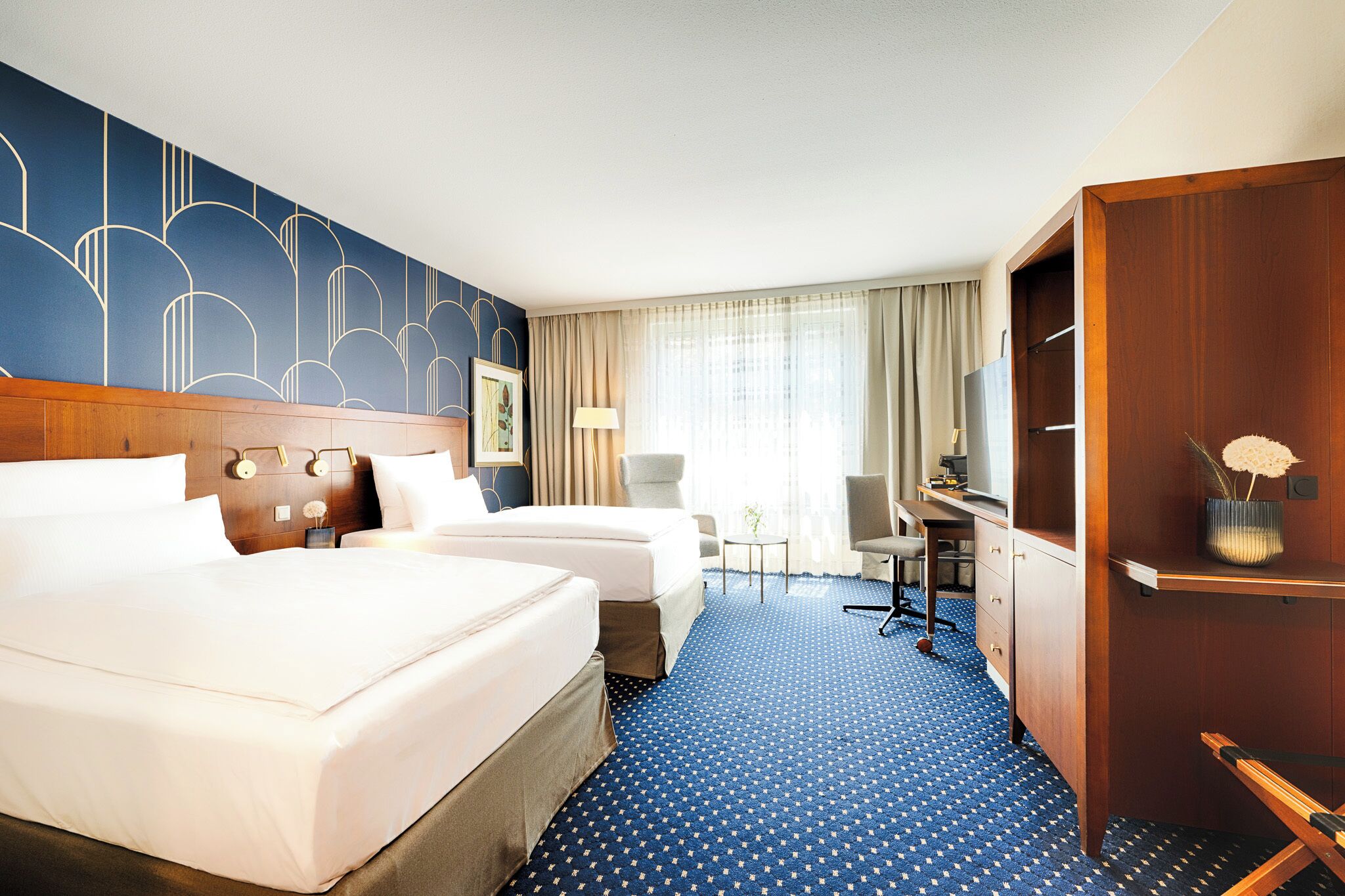 Een hotelkamer met twee bedden, een bureau, een stoel, een lamp en een kledingkast.