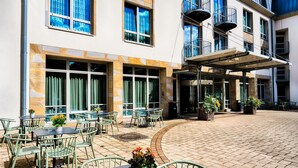 Ein Außenbereich mit Terrassenmöbeln, ein überdachter Sitzbereich und ein Gebäude mit großen Fenstern und Balkonen.