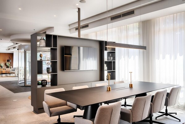 Una sala de reuniones moderna con una mesa grande, sillas, un televisor montado y estanterías empotradas.