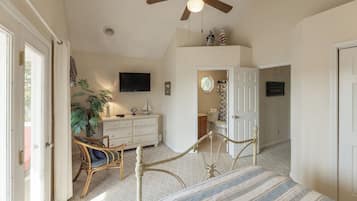 Een slaapkamer met een bed, een dressoir, een televisie, een plafondventilator en een deur naar een badkamer.
