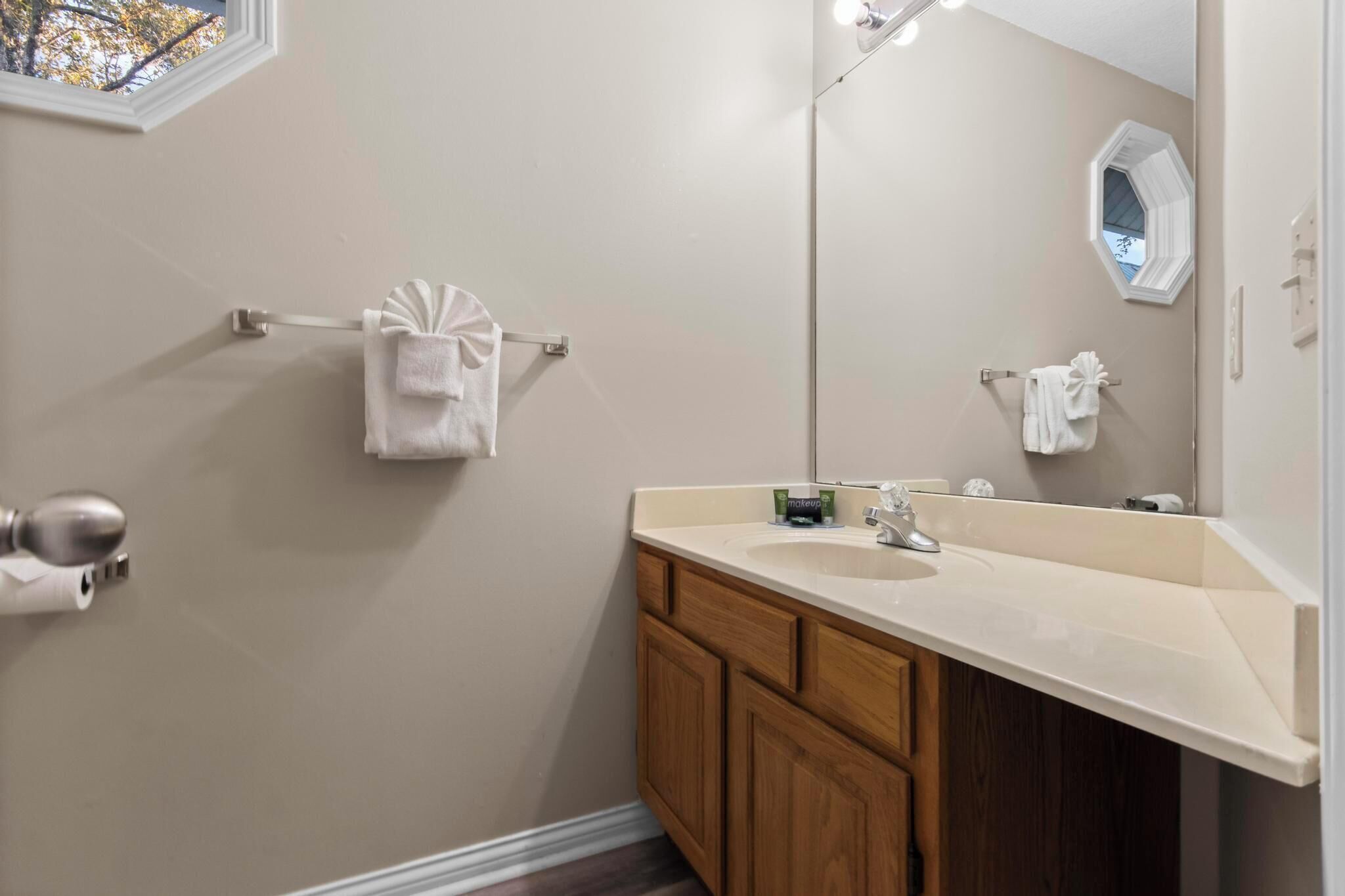 A bathroom with a large mirror, a sink, wooden cabinets, and two towel racks.