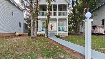 A two-story house with a porch, a driveway, and trees.