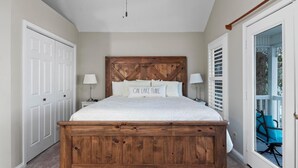 A bedroom with a wooden bed frame, white bedding, and a view of the outdoors through a sliding glass door. - Two Bedroom Harbor View Condo (Grand Rivers)