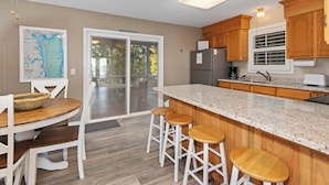 A kitchen with a granite countertop, wooden cabinets, a refrigerator, and a dining area with a table and stools. - Two Bedroom Harbor View Condo (Grand Rivers)