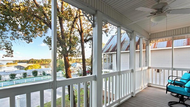 A covered porch with a view of a lake, trees, and a building with a metal roof. - Two Bedroom Harbor View Condo (Grand Rivers)