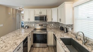 Eine moderne Küche mit weißen Schränken, einer Granit Arbeitsplatte, einem eingebauten Backofen, einer Mikrowelle und einer Edelstahl-Spüle.