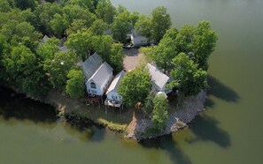 An aerial view of a secluded house surrounded by dense trees and a body of water, with a dock extending into the water.