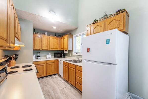 A kitchen with wooden cabinets, a white refrigerator, a stove, a microwave, and a sink.