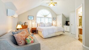 A bedroom with a large bed, a ceiling fan, a window, and a TV in the corner.