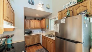 A compact kitchen with wooden cabinets, a stainless steel refrigerator, a microwave, and a sink.