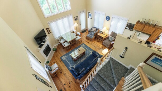 A spacious living area with a sofa, coffee table, and dining table. A staircase leads to a second floor. - Two Bedroom Bayside Condo (Grand Rivers)