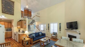 A spacious living area with a staircase, wooden furniture, a dining table, and a television. - Two Bedroom Bayside Condo (Grand Rivers)
