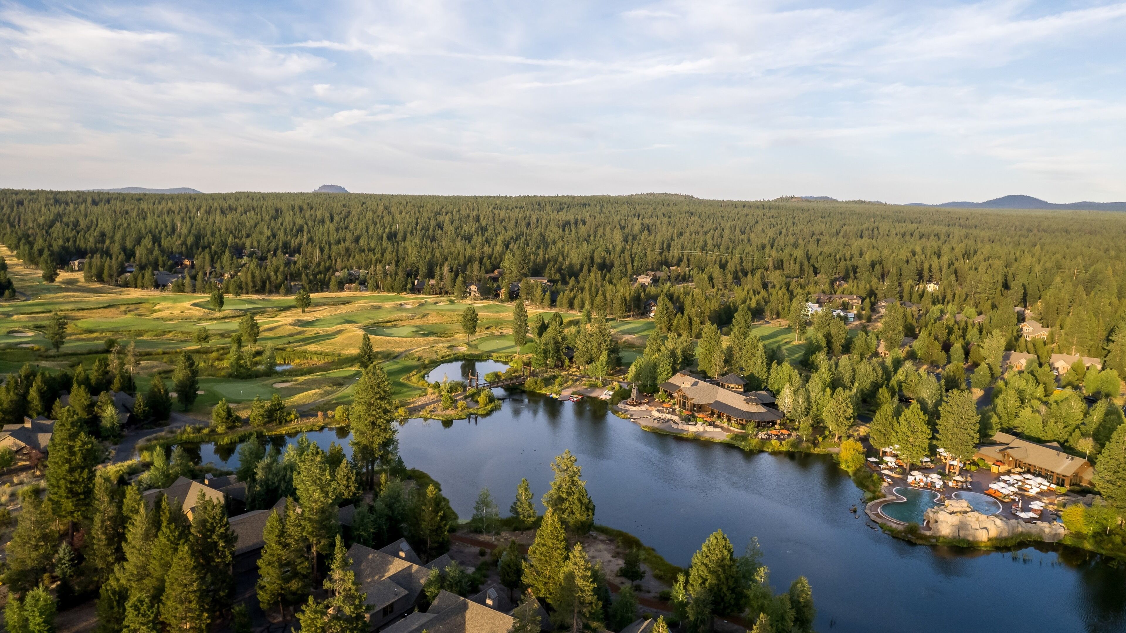 A golf course with a lake, surrounded by dense forest and residential buildings.