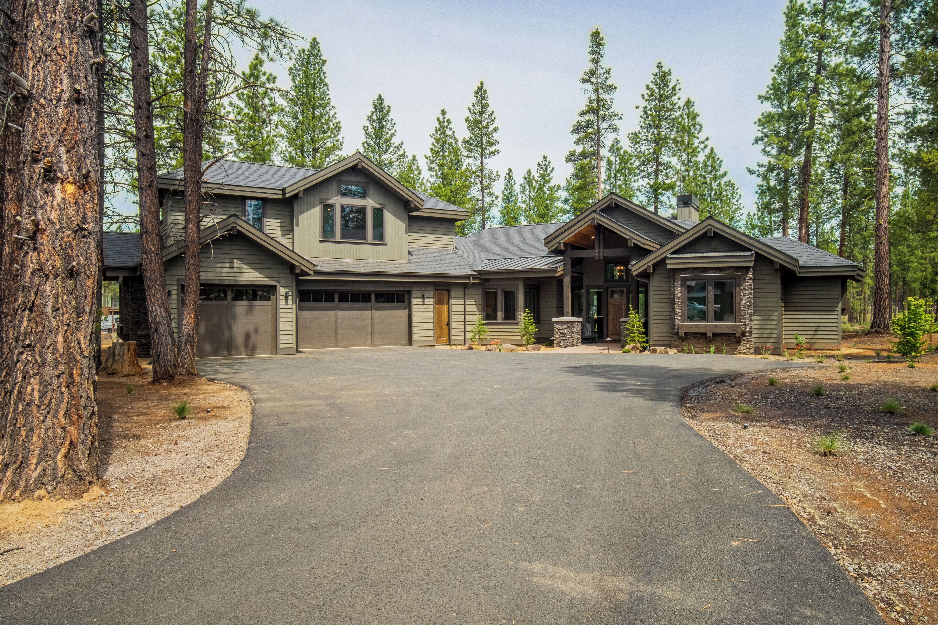 A two-story house with a garage, surrounded by tall pine trees.