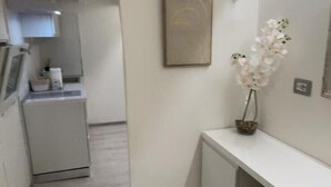 Ein schmales Entree mit einer Küchenzeile links, einem weißen Konsolentisch mit Blumen in einer Vase rechts und einem gerahmten Bild an der Wand.
