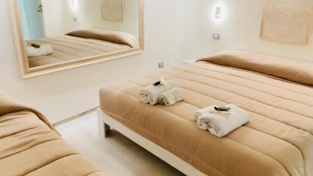 Ein modernes Schlafzimmer mit einem großen Bett, einem kleinen Sofa, einem Spiegel und einer Wandleuchte.