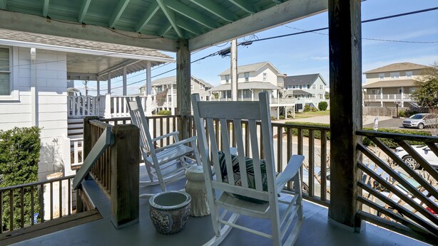 A covered porch with a white rocking chair, a small table, and a decorative bowl.