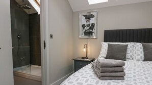 A modern bedroom with a geometric-patterned bedspread, a framed artwork above the bed, a bedside lamp, and a glass-enclosed shower area. - Brimstone (Ulverston)
