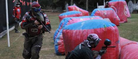 A group of people engaged in a paintball game, with inflatable barriers and trees in the background.