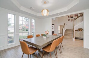 A dining area with a wooden table and orange chairs, large windows, and a staircase leading to another level.