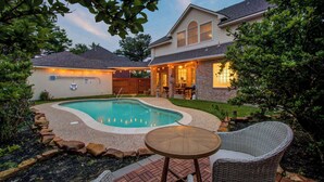 A backyard with a swimming pool, a covered patio, and a dining area.