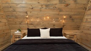 Una habitación con paneles de madera, una cama, dos mesitas de noche y luces de hadas.