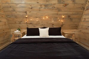 Une chambre confortable avec un plafond en bois, un lit avec une literie noire et blanche, et des guirlandes lumineuses.