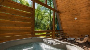 Una cabaña de madera con jacuzzi, mobiliario exterior y vistas a un bosque.