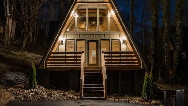 Una cabaña de madera triangular con una escalera central, ventanas amplias y un porche.
