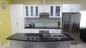 A modern kitchen with white cabinets, a stainless steel refrigerator, and two bar stools. - The Shack at Stansbury - Short walk to the beach! Off peak special! (Stansbury)