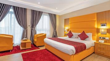 A modern hotel room with a large bed, a wooden nightstand, a desk, and a chair.