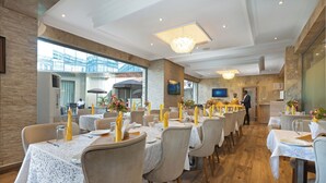 A restaurant with multiple tables set with white lace tablecloths, yellow napkins, and floral centerpieces. - Watercress Hotels and Signature (Lagos)