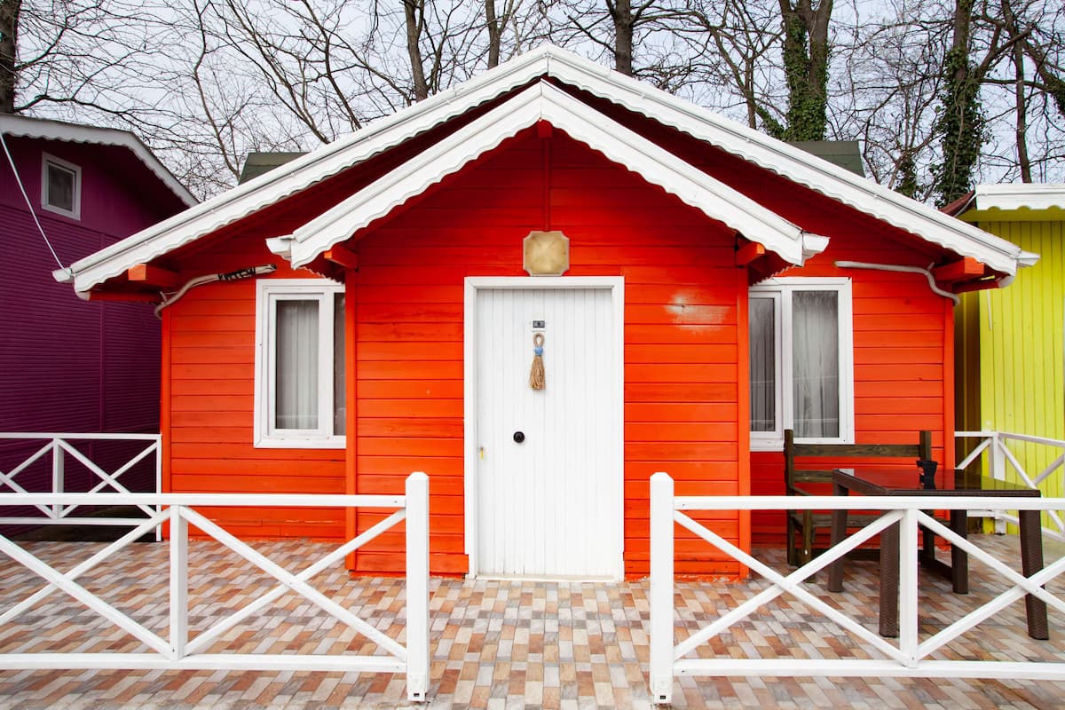 A red wooden cabin with a white door, a small porch, and a white fence.