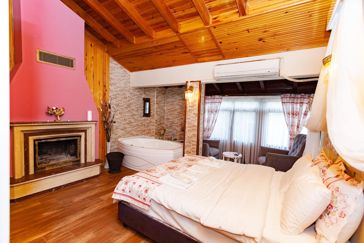 A bedroom with a large bed, a fireplace, a bathtub, and a small table.