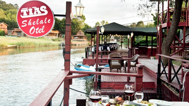 A riverside dining area with tables and chairs, a covered seating area, and a sign reading "TIAS Shelae Otel". - Ağva Tias Shelale Otel (Sile)