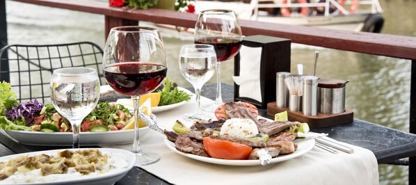 A dining table with plates of food, glasses of wine, and a view of a body of water. - Ağva Tias Shelale Otel (Sile)