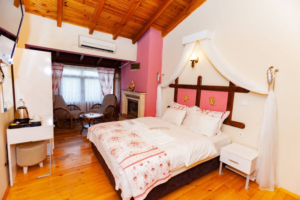 A bedroom with a wooden ceiling, a bed with a canopy, a small table with chairs, and an air conditioning unit.