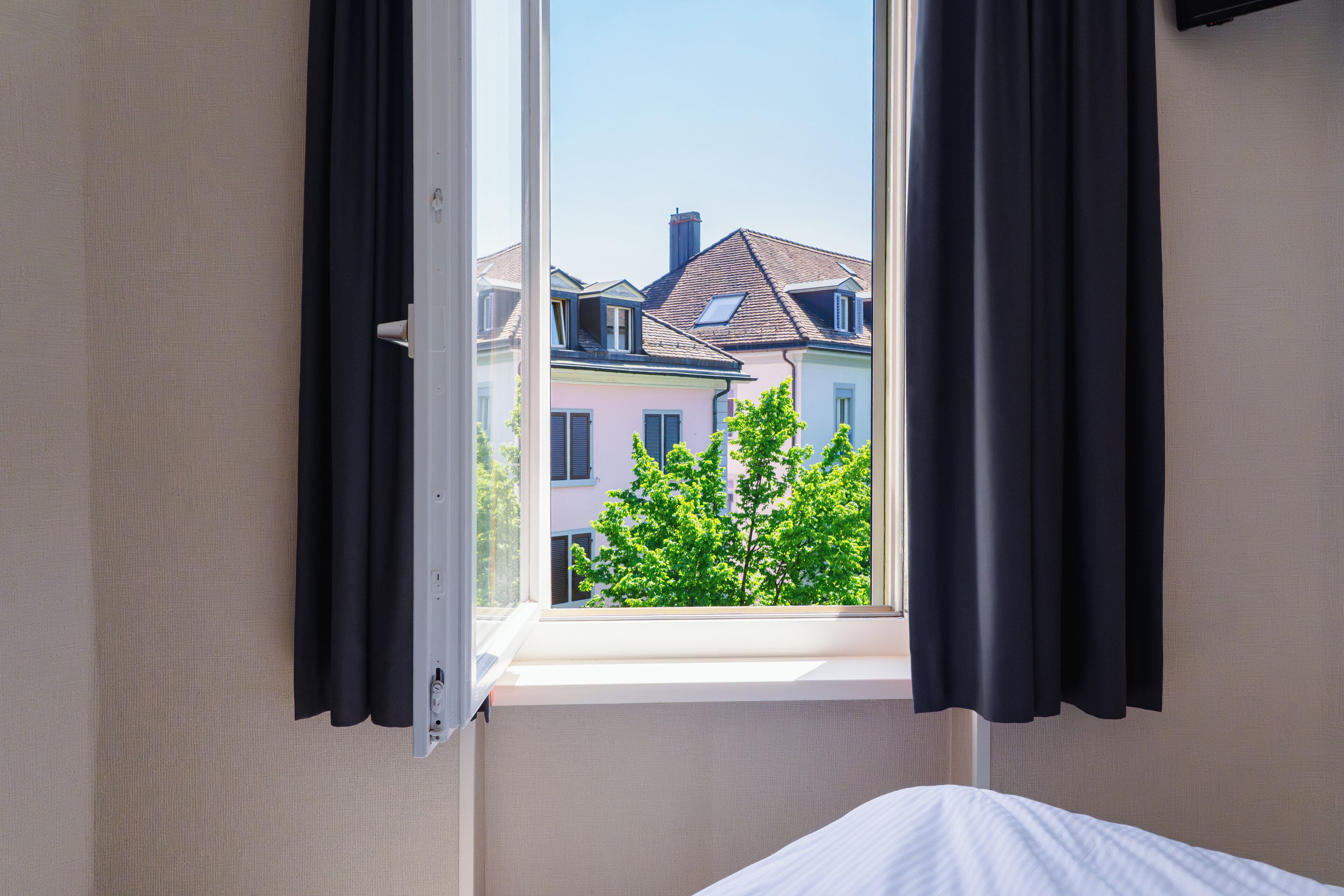 Une chambre d’hôtel avec une fenêtre donnant sur les bâtiments voisins et un arbre.