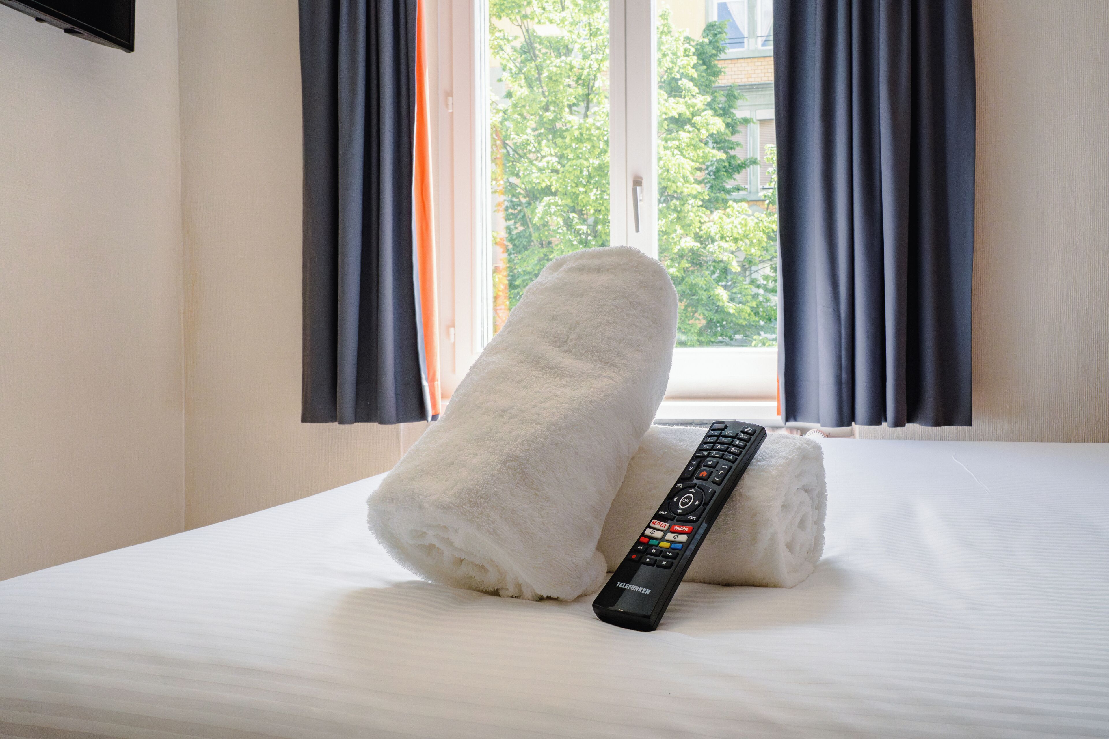 A neatly made bed with a rolled white towel and a remote control on it.