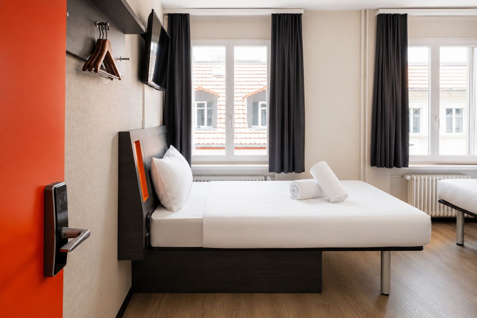 Una camera d'albergo moderna con un letto, una televisione e vista sugli edifici.