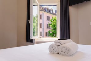 A hotel room with a bed, a window with curtains, and a view of a building outside. - easyHotel Zurich City Main Station (Zürich)