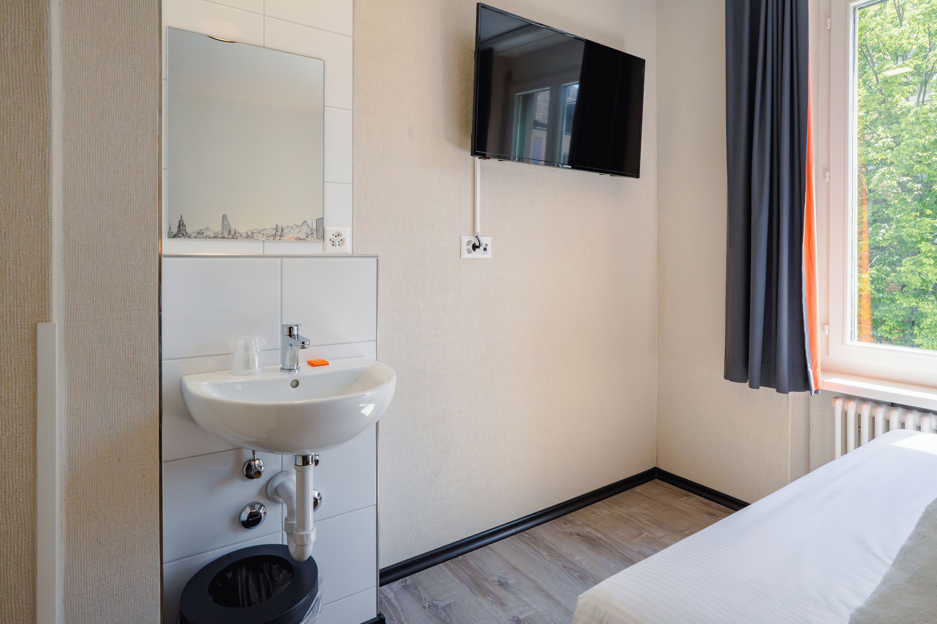 Ein Hotelzimmer mit einem weißen Waschbecken, einem Spiegel und einem an der Wand befestigten Flachbildfernseher.