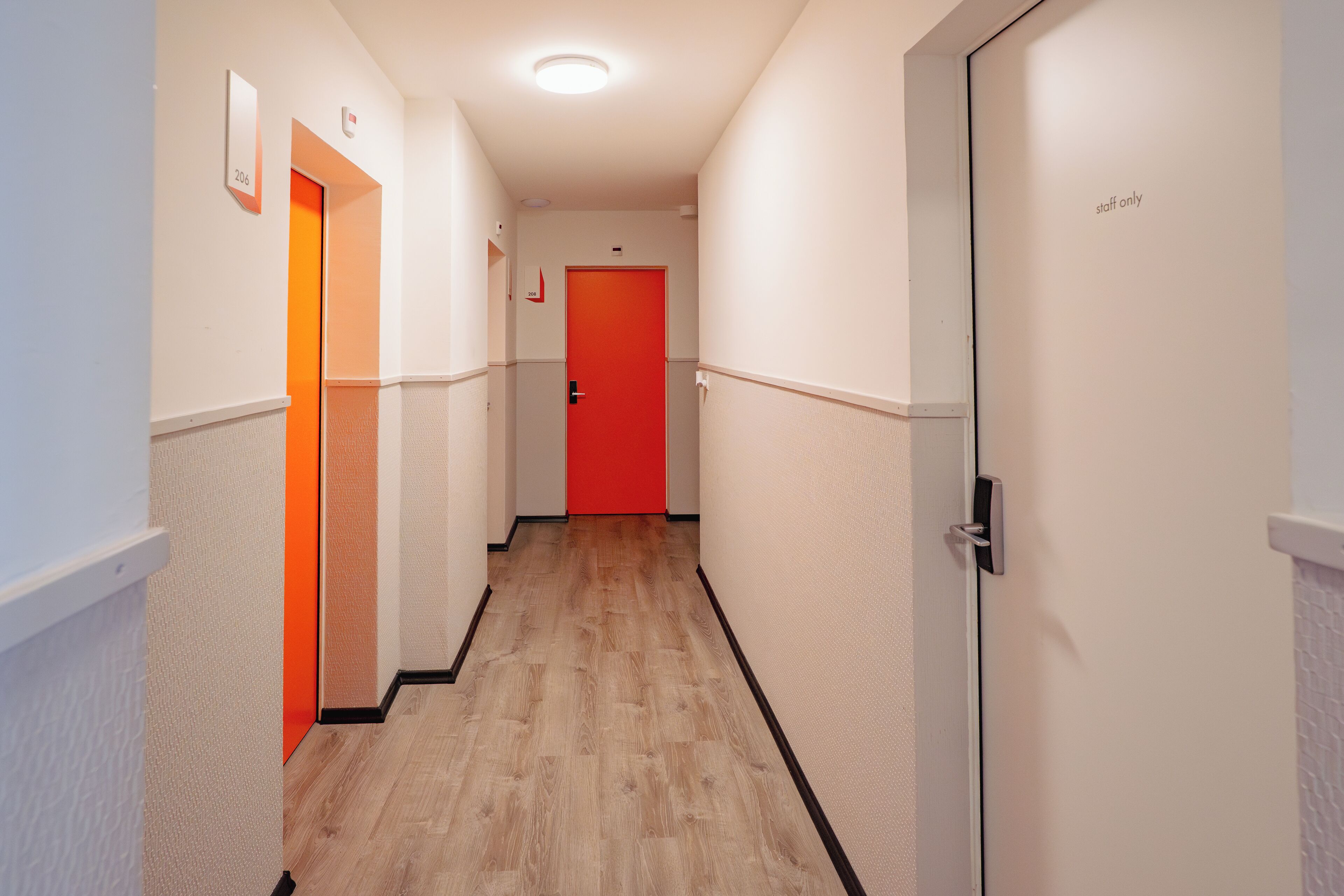 A hallway with a wooden floor, white walls, and doors with numbers.